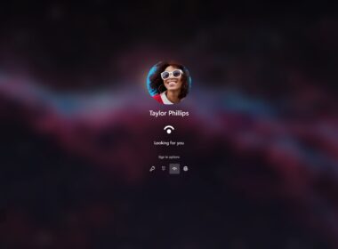 Prihlasovacia obrazovka Windows 11 na tmavom rozostrenom pozadí, v strede kruhový profilový obrázok usmievajúcej sa ženy v bielych okuliaroch, pod ním meno Taylor Phillips, ikona snímania tváre a text „Looking for you“, nižšie možnosti prihlásenia – kľúč, PIN, tvár a odtlačok prsta; vľavo dole zoznam používateľov, vpravo dole Wi-Fi, prístupnosť a vypnutie.