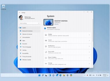 Okno Nastavení Windows 11 otvorené na stránke Systém, s bočnou ponukou položiek ako Bluetooth a zariadenia, Personalizácia či Windows Update a s dlaždicami Obrazovka, Zvuk a Oznámenia; pod oknom je panel úloh so zarovnanými ikonami v strede.
