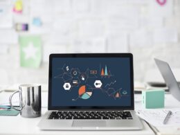 Notebook s grafmi na obrazovke na neupratanom pracovnom stole